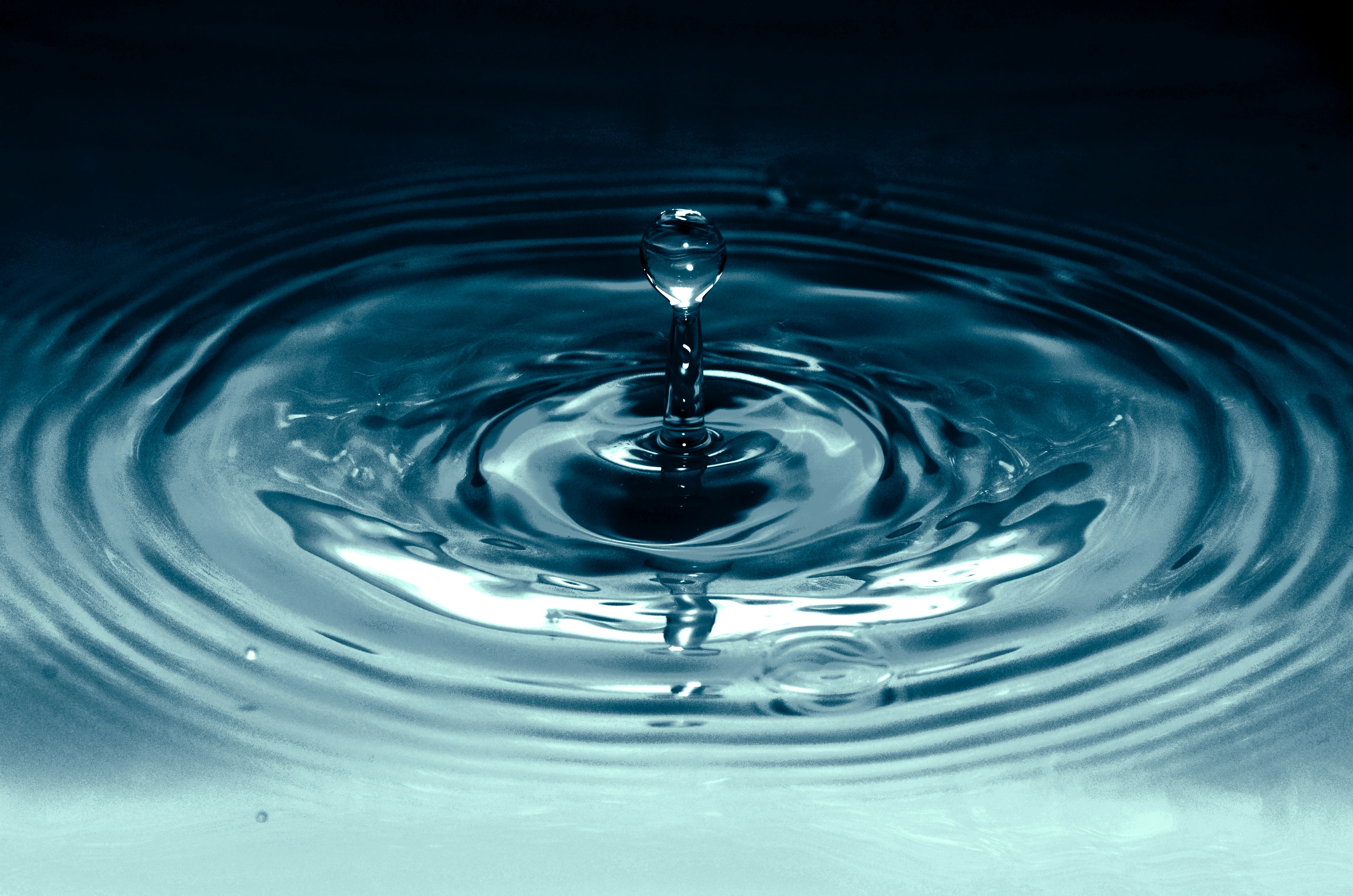 A single water droplet creating concentric ripples across a still, dark blue surface